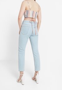 Ljusblå högmidjade jeans med rak passform och bakfickor, i kombination med en randig kortärmad topp och vita klacksandaler.