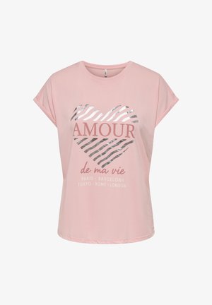 Joven mujer de pie con una camiseta rosa con diseño y texto, y pantalones cortos negros con borde en forma de concha, combinados con sandalias negras deslizantes.