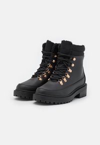 Bottes noires imperméables avec doublure en fausse fourrure, bout arrondi et quincaillerie dorée. Présentent un design à lacets et une semelle robuste pour une meilleure adhérence.