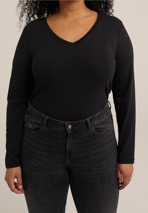 Sort langærmet top med V-hals design kombineret med højtaljede mørke denimjeans med frontknaplukning og lommer.