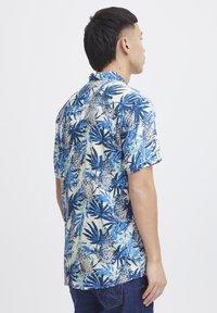 Camicia a maniche corte in blu e crema con un motivo di foglie tropicali e ananas. Realizzata in tessuto dalla superficie liscia e dalla vestibilità rilassata.