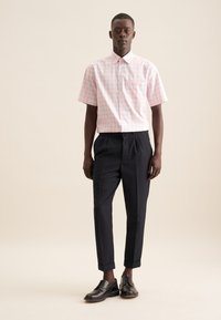 Camicia a maniche corte a righe rosa e bianche con taschino sul petto, abbinata a pantaloni neri su misura e scarpe nere stringate.