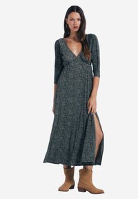Maxi kjole i mørkegrøn blomsterprint med trekvartærmer og en sideslids. Stylet med brune ankelstøvler. Blød stoftekstur.