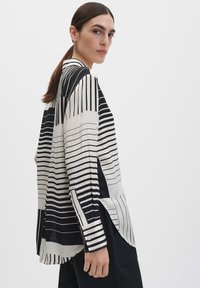 Schwarz-weiß gestreiftes Hemd mit langen Ärmeln, lockerem Schnitt und abgerundetem Saum. Der Stoff wirkt glatt mit einem glänzenden Finish.