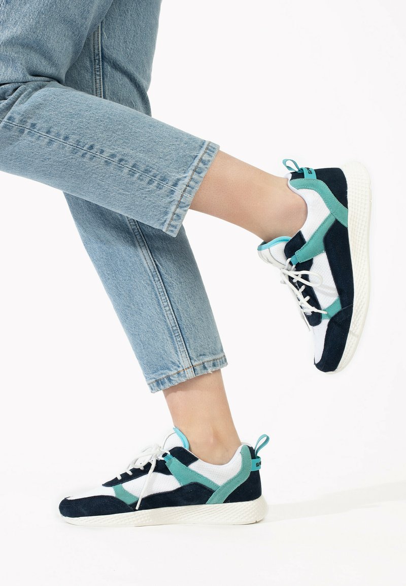 Marinblå och teal sneakers med övre del av mesh och mocka, vit sula och snördesign med en bakre hälflik. Bärs med avskurna jeans.