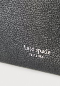 Carteira preta em couro com textura granulada e logótipo "kate spade NEW YORK" em relevo e acabamento metálico prateado. Design compacto e retangular.
