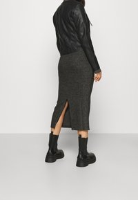 Černá kožená bunda přes šedo-pletenou sukně střední délky s bočním rozparkem. Modelka nosí černé robustní kotníkové boty. Hladká textura, úzký střih.
