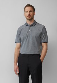 Grijs poloshirt met een subtiele textuur, contrasterende marineblauwe kraag en mouwafwerking, gecombineerd met zwarte broek. Knopen zijn duidelijk zichtbaar.