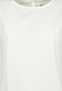 Blusa bianca, leggera, con una texture liscia. Presenta un colletto rotondo e una chiusura con bottoni sul retro. Design semplice, senza motivi o accenti.