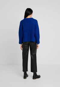 Dzianinowy niebieski sweter o prążkowanej fakturze, z okrągłym dekoltem i dopasowanymi rękawami, połączony z czarnymi skórzanymi spodniami i botkami za kostkę.