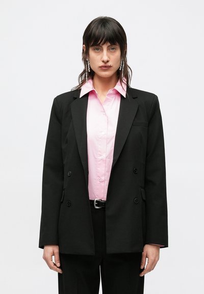 Black double-breasted blazer over a light pink button-up shirt. The outfit features long sleeves and a subtle sheen on the fabric.