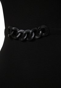 Gros plan d'une robe noire avec une large ceinture chaîne noire cintrant la taille, montrant la texture lisse du tissu et de grands maillons entrelacés.