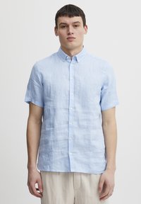 Camisa de botones de manga corta en azul claro, hecha de lino, con un acabado texturizado y un collar clásico, botones blancos y corte recto.