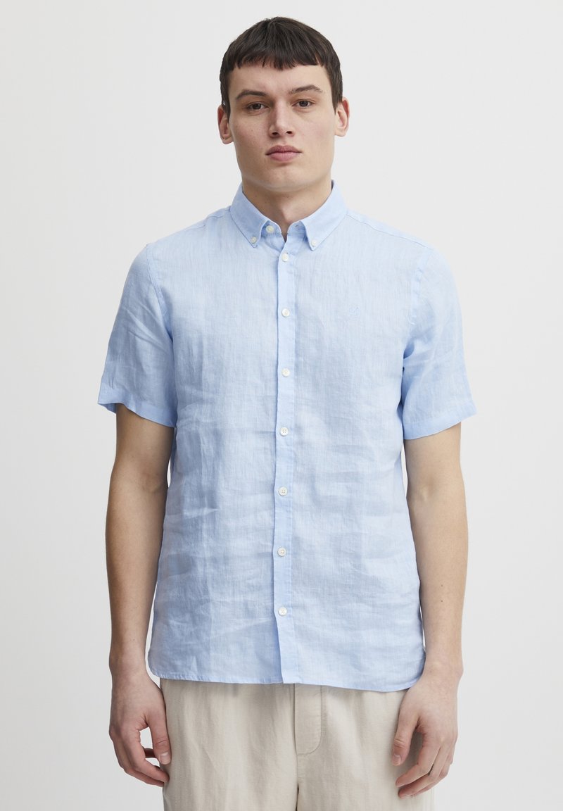 Camisa de botones de manga corta en azul claro, hecha de lino, con un acabado texturizado y un collar clásico, botones blancos y corte recto.
