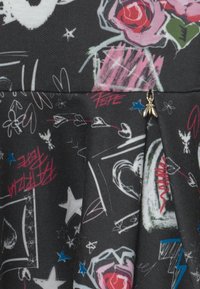 Schwarzer Stoff mit bunten Graffiti-ähnlichen Skizzen von Rosen, Sternen, Herzen und abstrakten Formen, mit einem kleinen goldenen Bienenanhänger.