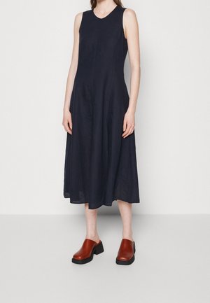 Sleeveless black midi dress worn with brown leather clogs with chunky black soles on a standing person against plain background.