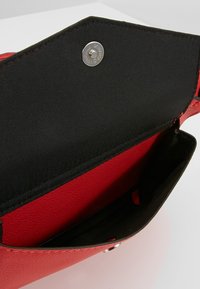 Borsa a tracolla rossa con texture, interna in tessuto nero. Caratterizzata da una chiusura a scatto metallica e un design a tasca aperta per un accesso facilitato.