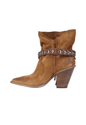 Stivaletto western alla caviglia in suede marrone con punta appuntita, tacco in legno impilato e cinturino decorativo in pelle con dettagli metallici intorno alla caviglia.