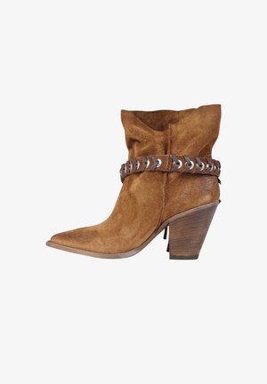 Stivaletto western alla caviglia in suede marrone con punta appuntita, tacco in legno impilato e cinturino decorativo in pelle con dettagli metallici intorno alla caviglia.