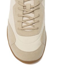 Baskets beige et beige clair avec des accents en daim, des lacets croisés et une semelle en caoutchouc, vues de dessus avec un focus sur la zone des orteils et des lacets.