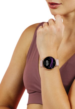 Orologio smart rotondo con cinturino rosa e accenti metallici. Il display digitale mostra l'ora e elementi grafici viola. Indossato su un polso.