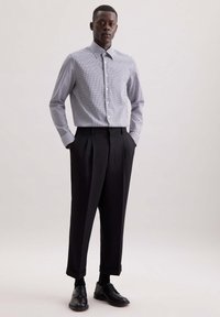 Zwart-wit geblokt overhemd met knopen, gecombineerd met hoogstaande zwarte broek met plooien en opgerolde mouwen, aangevuld met zwarte schoenen.