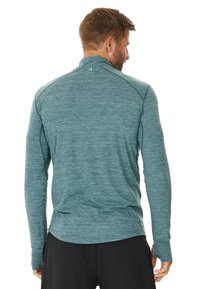 Langarmshirt van een textuurrijke teal stof, met een hoge kraag, raglanmouwen en platte naden voor comfort tijdens het dragen.