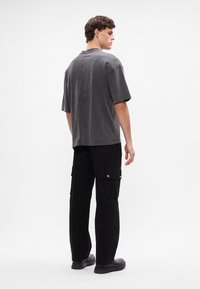 Graues oversized T-Shirt mit kurzen Ärmeln, Rückennahtdetails, kombiniert mit schwarzen Cargo-Hosen mit seitlichen Taschen und silbernem Zubehör.
