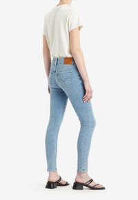 Ljusblå högmidjade skinny jeans med en beige läderlogotyp, ihopparat med en krämfärgad t-shirt med korta ärmar och svarta klacksandaler.
