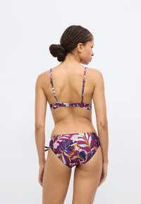 Bikini deux pièces avec un motif floral dans des tons de violet, rose et vert. Comprend des bretelles ajustables et un détail noué sur le côté du bas.