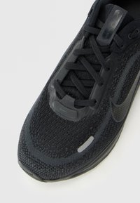 Mustad mustad Nike jooksujalats, millel on võrgusilmast ülemine osa, mustad paelad ja peened peegeldavad detailid varvaste ja külje peal.