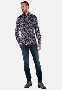 Langärmliges schwarzes Hemd mit floralem Muster in Lila und Pink, kombiniert mit dunkelblauer Jeans und braunen Schnürstiefeln.