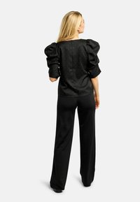 Čierna saténová blúzka s nafúknutými rukávmi a ozdobnými striebornými bodkami, skombinovaná s voľnými čiernymi nohavicami. Hladká textúra a klasický strih.