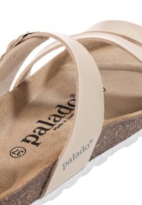Beiga sandaler med två glansiga korskonstruktioner, en korkfotbädd och en texturerad vit sula. Har "palado"-logotypen på innersulan.