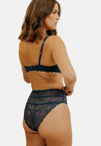 Soutien-gorge en dentelle bleu marine et culottes taille haute avec motif floral. Dispose de bretelles réglables et de bords festonnés. Texture semi-transparente.