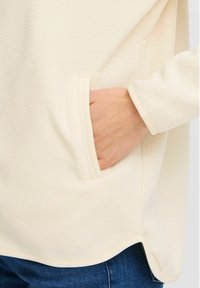 Kreemivärvi fleece-pulkuga, küljetasku ja kontrastse äärega. Omab vabalt langevat istuvust ja ümarat serva. Pehme tekstuur, minimaalne disain.