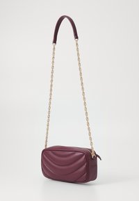 Burgundy nahkalaukku, jossa on tikattu muotoilu, kultaketjuolkaimet ja suorakulmainen muoto, jossa on vetoketjukiinnitys. Silkkinen pinta ja yksityiskohdat.