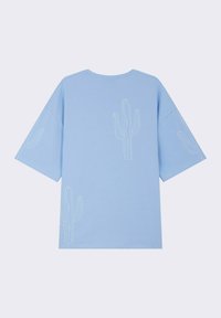 Camiseta de algodón de color azul claro con mangas cortas, que presenta diseños de cactus bordados en blanco en la parte delantera y trasera. Corte relajado, cuello redondo.