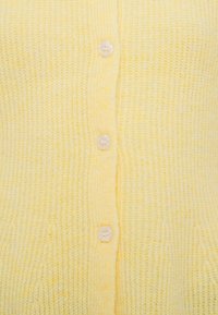 Dzeltena adīta kardigana ar fakturētu rakstu, pieciem maziem baltiem pogām priekšpusē un apkakli ar pogu.
