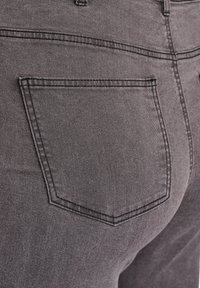 Jean en denim gris avec une poche arrière au design pointu, des détails de couture subtils et une finition lisse légèrement texturée.