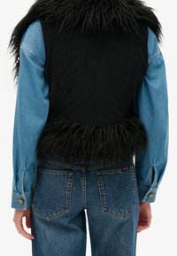 Jeansjacka med svart fuskpälsdetalj, med en kortad stil, blå ärmar och knapppyser på ärmsluten, som visar en tvåfärgad design.