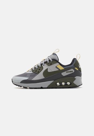Niskie buty sportowe Nike Air Max w kolorze szarym i oliwkowozielonym z czarną podeszwą, widoczną amortyzacją powietrzną i żółtymi akcentami.
