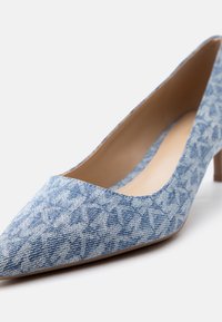 Μπλε ύφασμα με μυτερή μύτη, ψηλό τακούνι με διακριτικό γεωμετρικό μοτίβο και χαμηλό τακούνι στιλέτο σε λευκό φόντο.