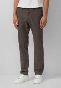 Donkerbruine, gestructureerde broek met een subtiel verticaal streepjespatroon, voorzien van een knoopsluiting, riemlussen en een slim fit. Gecombineerd met witte sneakers.