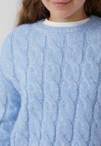 Hellblauer, kabelgestrickter Pullover mit Rundhalsausschnitt, der erhöhte Wellenmuster und einen weichen, strukturierten Stoff aufweist. Keine sichtbaren Beschläge oder Akzente.