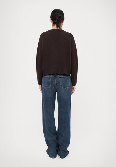 Brown cropped sweater with ribbed hem worn over loose-fitting, high-waisted blue jeans, featuring a classic five-pocket design and faded texture.