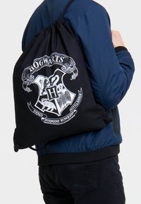 Black drawstring bag featuring a white Hogwarts crest design with various mythical creatures and text, made from a lightweight fabric.