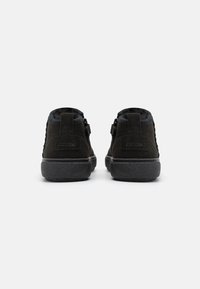 Zapatos negros de ante de caña alta con lados texturizados, punteras redondeadas y suelas de goma. Incluyen tiradores traseros para facilitar su uso.
