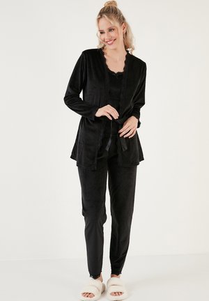 Black velvet loungewear set featuring a long cardigan with lace trim, matching pants, and fuzzy white slippers; soft texture and relaxed fit.
