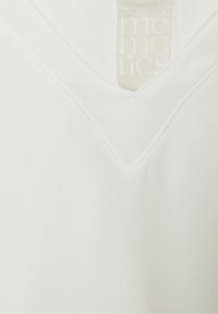 Top a V in morbido tessuto bianco, con cuciture pulite e una leggera lucentezza. L'etichetta riporta "colleziona ricordi" con un design leggermente impresso.